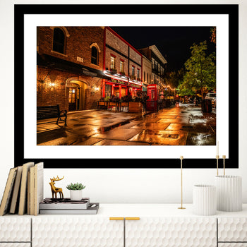 A photograph of night photography of Poppy and Parliament restaurant in Downtown Huntsville featuring a glowing red phone booth and rain-lit street hanging on a wall.