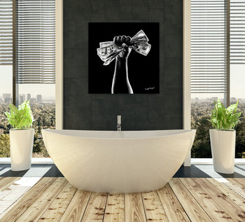A black and white canvas painting depicting a raised fist holding a dollar sign, displayed above a bathtub in a room with wooden flooring and two potted plants.