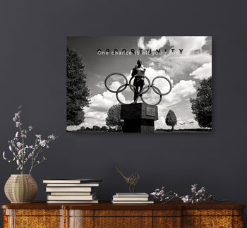 A canvas print featuring a black and white image of a statue with the text 'One chance is all you need.' - Jesse Owens on it, displayed on a wall above a decorative shelf with books and a vase.