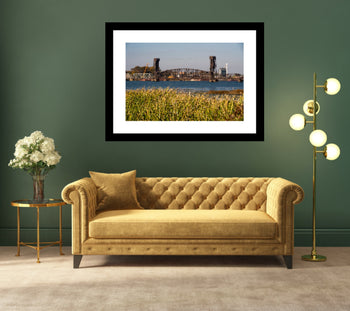 Waterfront photograph of Decatur Railroad Bridge with yelow and green grass in foreground mounted on a wall above a yellow sofa. 