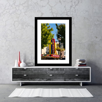 A framed canvas print of the Princess Theater, displaying a colorful building with a marquee, framed on a wall console table.