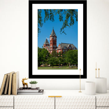 A framed art print featuring Samford Hall, Auburn University, with a clear blue sky and greenery in the background.