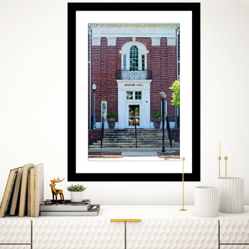A framed art print of Ingram Hall, Auburn University, displayed on a wall above a bookshelf with decorative items.