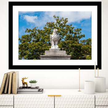A framed art print featuring a photograph of the War Eagle statue at Auburn University, displayed on a wall above a bookshelf with books and decorative items.