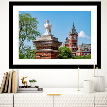 A framed art print featuring a photograph of Auburn University campus, showcasing a statue and buildings with a clear blue sky.