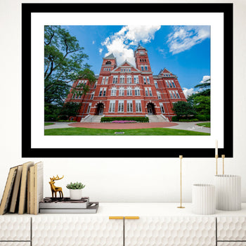 A framed art print of Samford Hall, Auburn University, displayed on a wall above a bookshelf with a few decorative items.