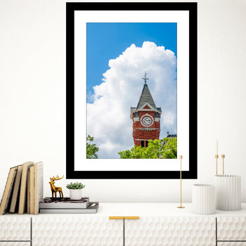 A framed photograph of Auburn University's Samford Hall with a blue sky and clouds in the background, displayed on a wall above a bookshelf.