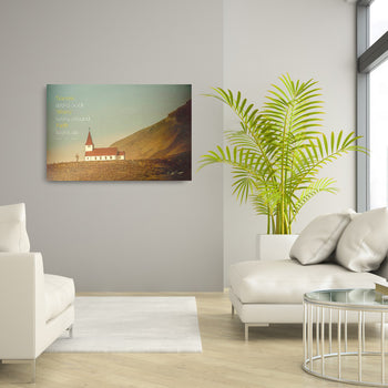 A canvas print featuring a church in a mountainous landscape, hung on a wall in a bright living room setting.