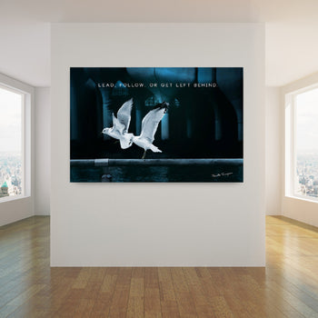 A canvas print featuring two birds in flight with text overlay 'LEAD, FOLLOW, OR GET LEFT BEHIND' on a dark background, displayed on a wall.