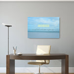 A canvas print with a image of a bird flying above water, hung on a wall over a desk with a chair and lamp.