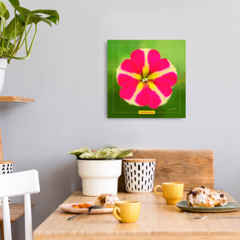 A square canvas art print with a vibrant image of a pink flower, displayed on a wall above a wooden table with plants and cups.