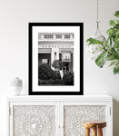 A black and white photo of the Huntsville Museum of Art building, framed in a white frame, displayed on a white wall.