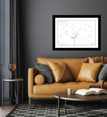 A black and white photo of birds flying around a light post displayed on a wall above a brown sofa with beige cushions.