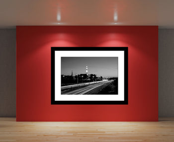 A framed black and white photograph of a rocket launch site displayed on a red wall, with a mat and frame not included.