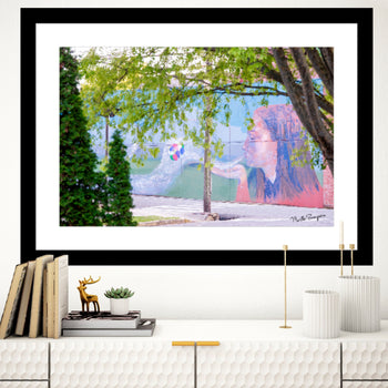 A framed graffiti wall print featuring a colorful artistic depiction of a female figure with a background of trees and buildings.
