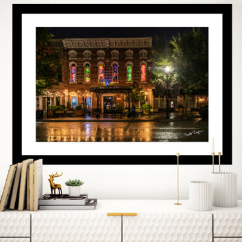 A framed fine art print featuring a photograph of a rainy night in downtown Huntsville, Alabama, with illuminated storefronts and a wet street.