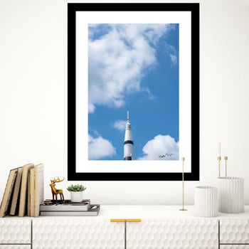 The towering white and black spacecraft stands as a powerful symbol of innovation, exploration, and our endless quest to reach beyond Earth. Set against a backdrop of fluffy white clouds and an expansive, brilliant sky, the image evokes a feeling of limitless possibilities and grand achievement.