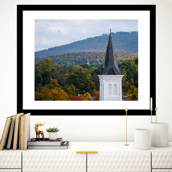 A framed art print depicting a church steeple with a scenic view in the background, displayed on a wall in a modern interior setting.