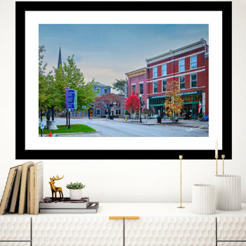 A framed photography print depicting a downtown Huntsville scene with a church steeple, displayed on a wall above a bookshelf with a few decorative items.