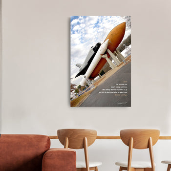 A canvas print featuring a rocket and spacecraft with a quote by Wernher Von Braun mounted on a wall, with two chairs in front of it.