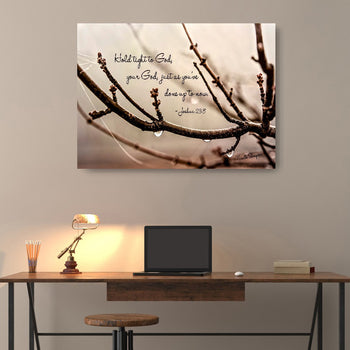 A framed inspirational canvas with a scriptural quote displayed on a wall above a desk with a laptop and lamp.