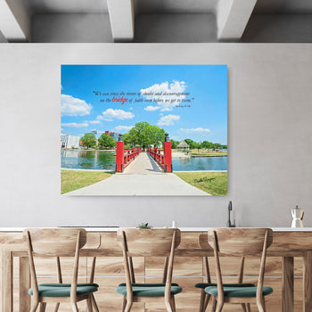 A framed inspirational canvas print depicting a red bridge over a river, displayed on a wall above a counter stools and wooden table.