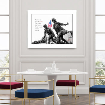 A framed print featuring a statue with an American flag, displayed on a wall above a modern white table with colorful chairs in a room with large windows.