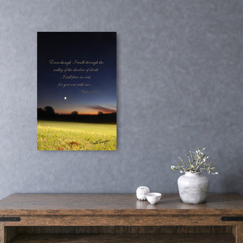 A framed inspirational poster with a scripture verse, displayed on a wall above a table with decorative items.