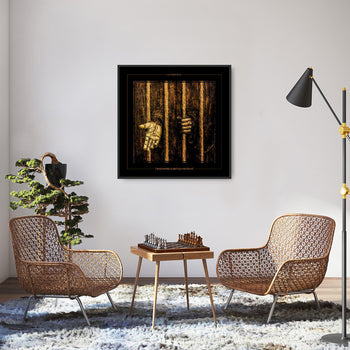 A framed artwork depicting a prison cell with a prominent golden cross on the wall, displayed on a wall above a small table between two modern-style chairs in a living room setting.