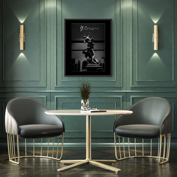 A framed print of Giambologna's Abduction of a Sabine Woman statue, displayed on a wall between two round chairs and under wall-mounted spotlights.