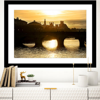 A framed art print featuring the Pont Neuf bridge in Paris with a black candelabrum, displayed on a wall above a modern white console table.