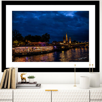 A fine art print featuring a night view of the Eiffel Tower and a bridge over the River Seine, with a calm body of water and a clear night sky.
