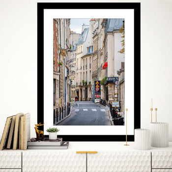 A framed art print featuring a narrow street in Paris with a person walking down the street, a 15km road sign, and Parisian architecture in the background.